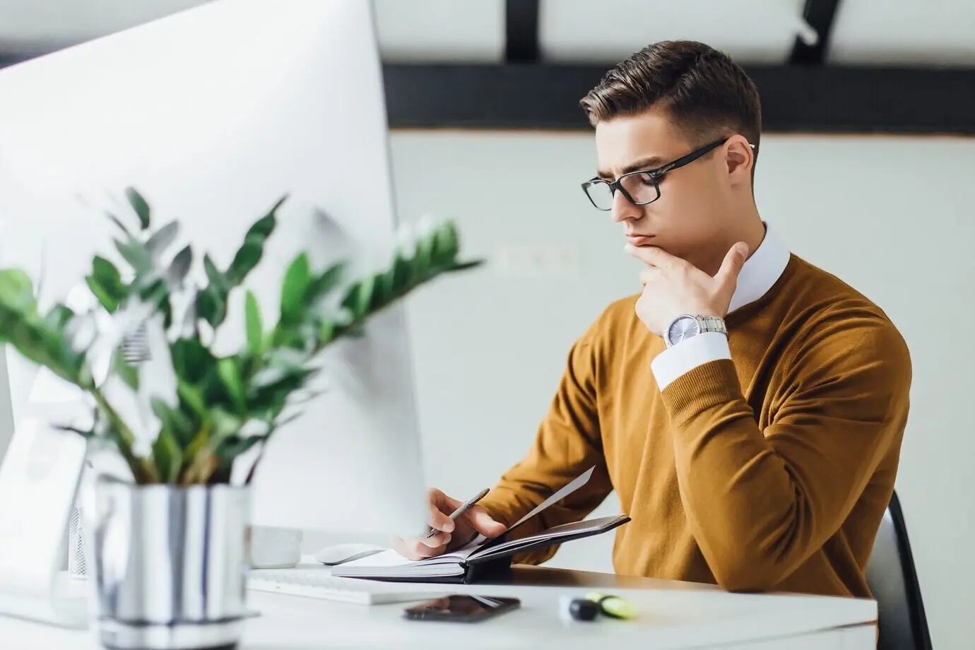 A good-looking, creative businessman with a laptop computer, writing notes in the office.