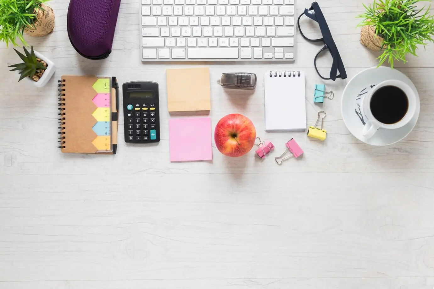 Overhead view of an apple and a coffee cup with office stationery on a white wooden desk.