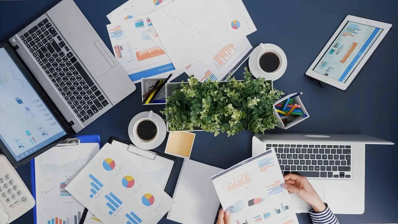 Top-down view of a female manager reviewing financial paperwork and strategy while typing expertly on a laptop.